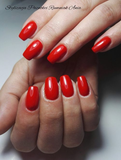 Close-up of hands with glossy bright red manicure on short oval nails across both hands, showing polished nails.