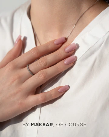 Close-up of a hand with pink nails, a silver ring, and a delicate necklace resting on a white shirt; watermark reads 'BY MAKEAR, OF COURSE'.