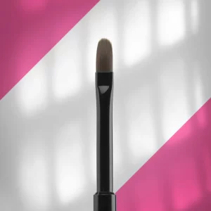 Makeup brush with beige bristles and a black handle standing upright against a pink-and-white diagonal background.