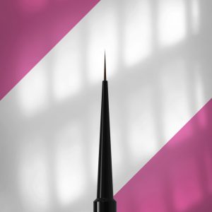 Close-up of a fine black eyeliner brush pointing upward against a pink and white diagonal background.