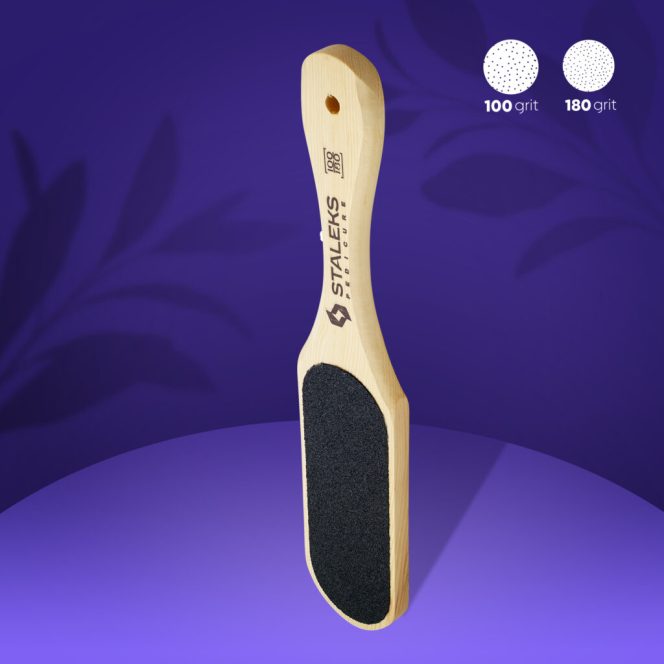 Wooden-handled foot file with a black abrasive pad for pedicures, dual-grit 100 and 180 shown in the corner on a purple background.