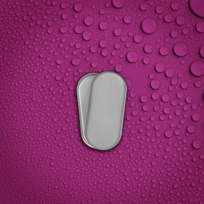 Two small stainless steel pill cases stacked together on a bright pink background covered with water droplets.