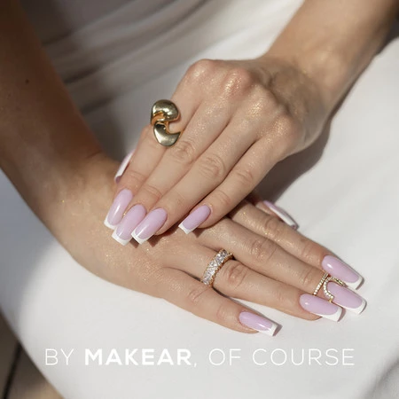 Close-up of hands with pale pink square nails, wearing a two-tone knot ring and a diamond-studded band on a white surface.
