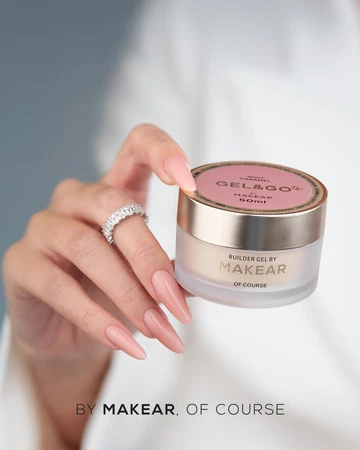 Close-up of a hand with long pink nails and a ring holding a small frosted makeup jar with a pink lid, branded Makear.