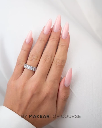 Close-up of a hand with long pink almond nails and a silver ring on the ring finger, resting on white fabric.